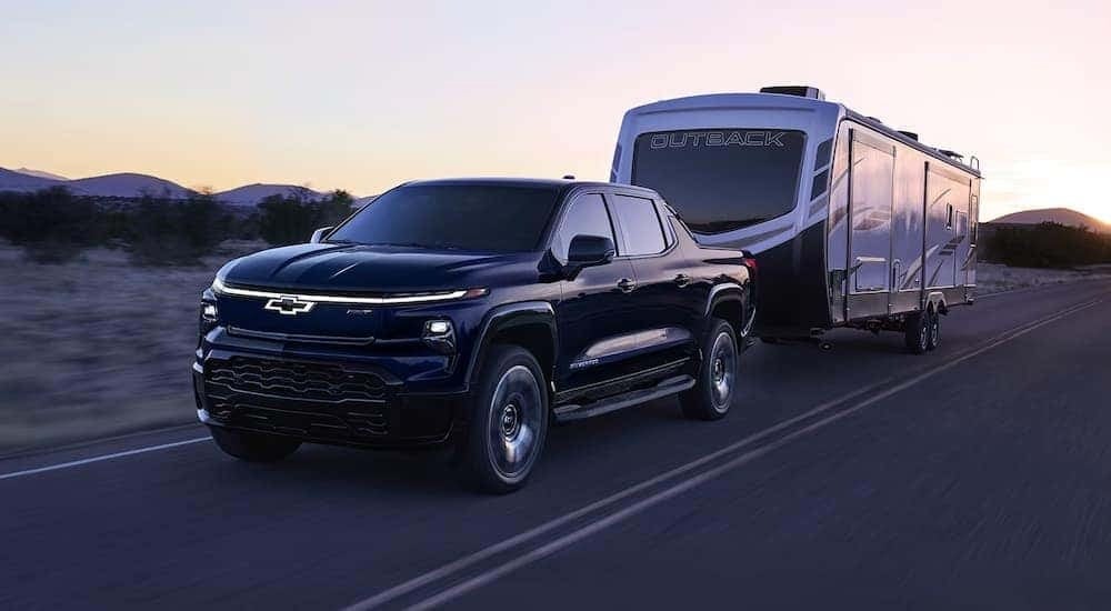 A black 2024 Chevy Silverado 1500 EV RST towing a large camper on an open road.