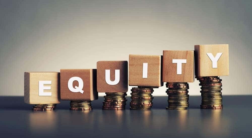 Equity is shown written on blocks while sitting on coins.