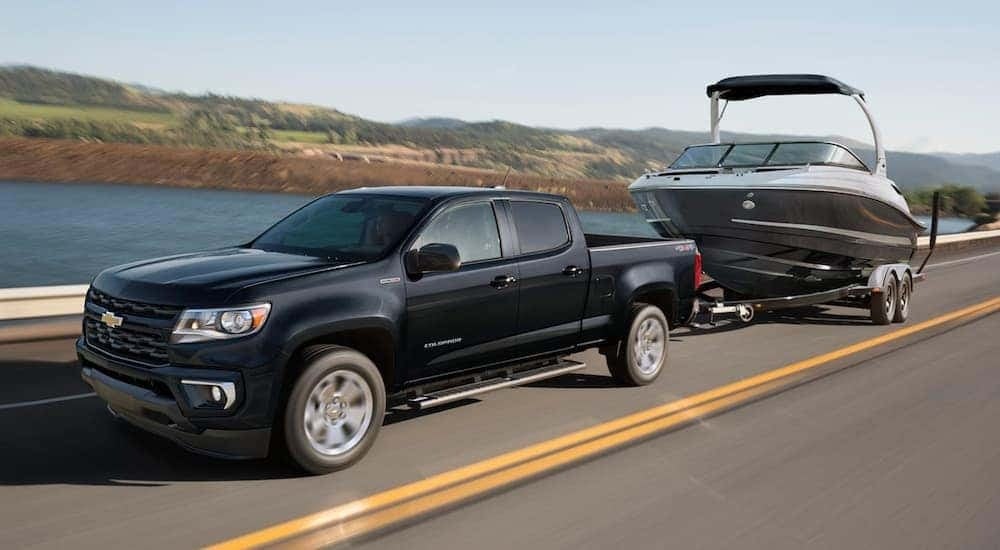 A black 2021 Chevy Colorado is shown towing a boat near a lake.
