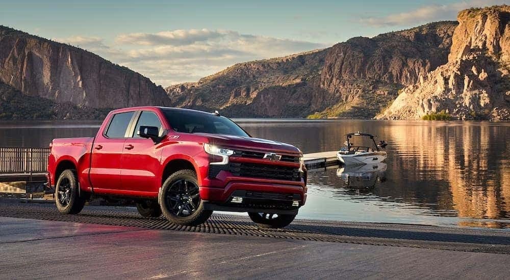 A red 2025 Chevy Silverado 1500 RST parked at a lakeside boat launch.