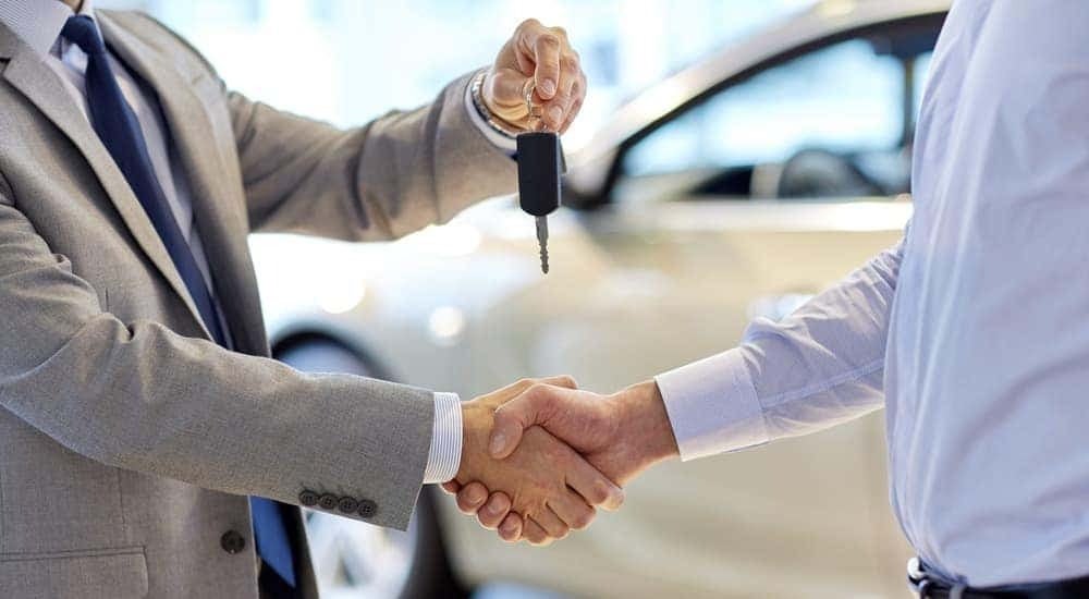 A car salesman is shown handing a key to a customer who searched for "sell my car."