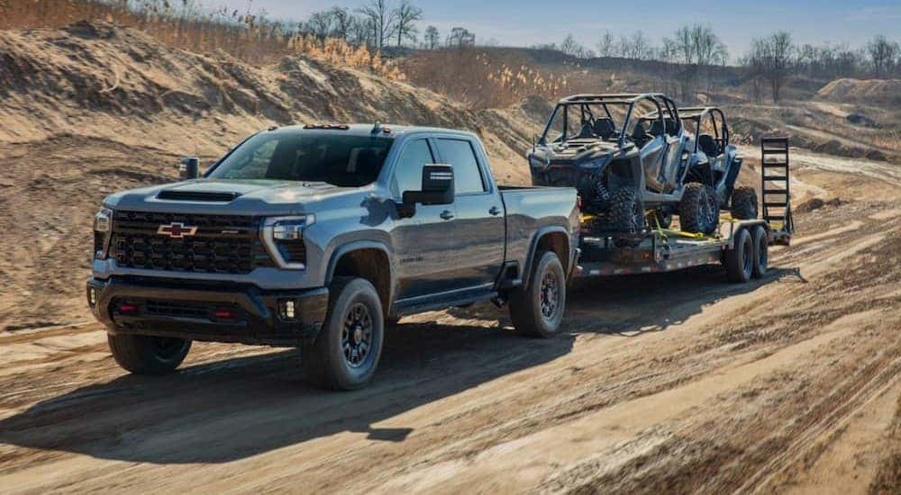 A gray 2024 Chevy Silverado 2500 HD is shown towing a trailer off-road.