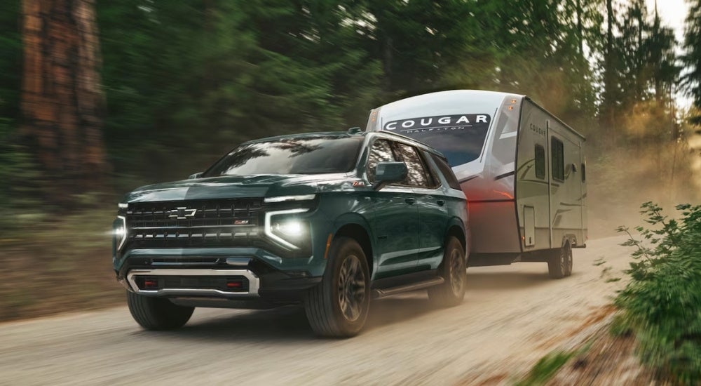 Green 2026 Chevy Tahoe Z71 towing a camper down a dirt road