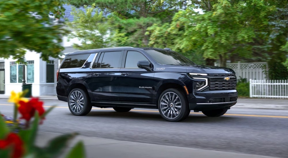 Dark blue 2025 Chevy Suburban High Country driving past a white picket fence
