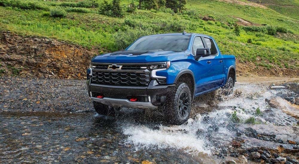 A blue 2022 Chevy Silverado 1500 ZR2 is shown off-roading through a river after visiting a used Chevy truck dealer.