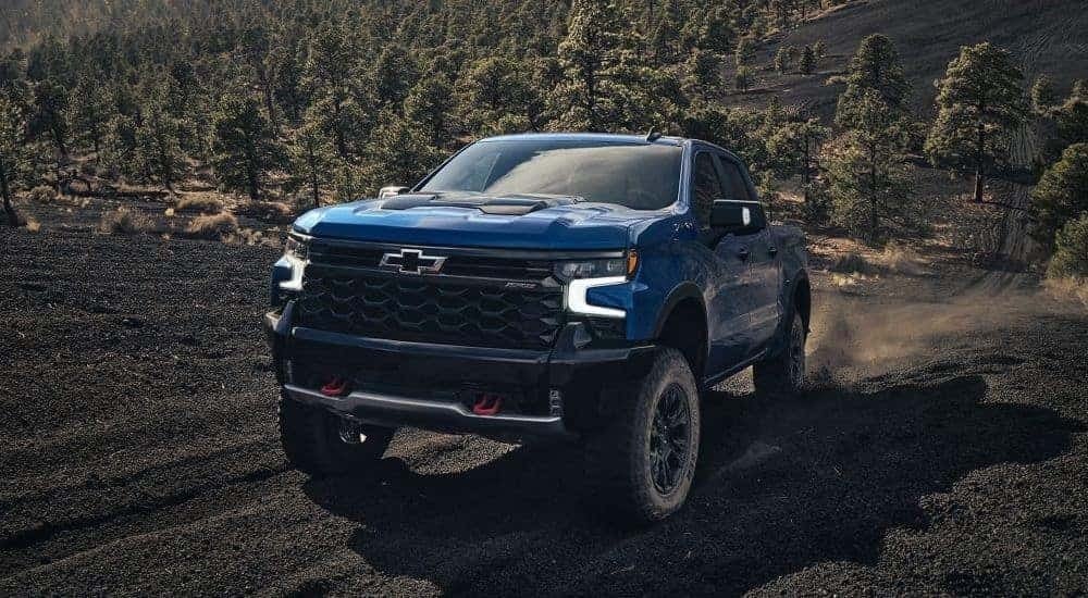 A blue 2024 Chevy Silverado 1500 ZR2 driving up a dirt hill.