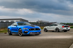 Two sporty cars, a blue and a silver one, parked on an overcast day. The setting is an industrial area with a sense of dynamic elegance.
