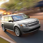 A silver SUV speeds along a blurred city street, conveying motion and urban energy. Sunlight casts a warm glow, highlighting the vehicle's sleek design.