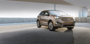 A bronze SUV is parked in a modern, open-air garage with a city skyline in the background. The morning light highlights the car’s sleek design, conveying elegance.
