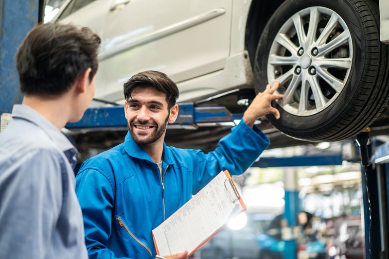 Service technician discussing a vehicle inspection with a customer beside a car on a lift.