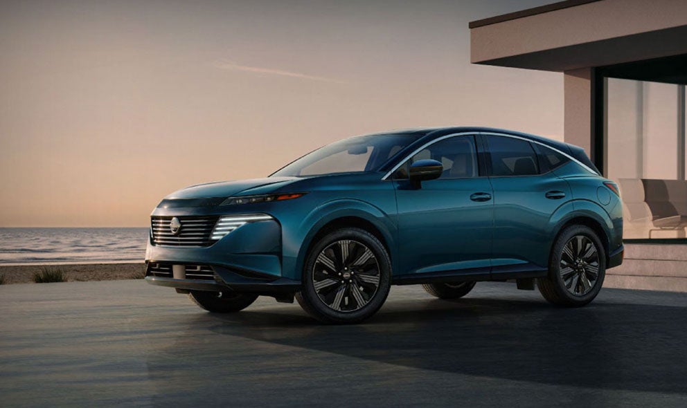 A sleek, modern blue crossover SUV parked on a driveway, with a beach and a building in the background.