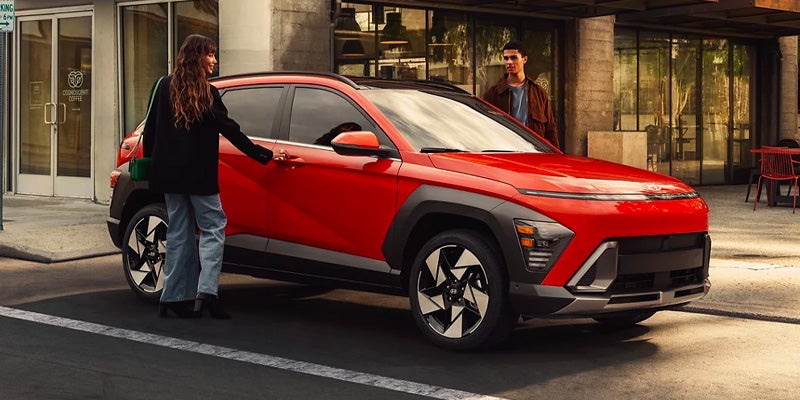 Woman approaching a red Hyundai SUV parked on a city street with a man standing nearby.
