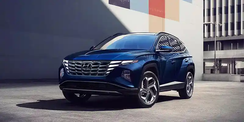 A blue Hyundai Tucson Hybrid SUV parked in an urban setting with modern architecture in the background.