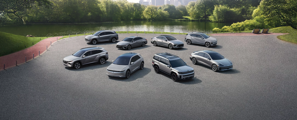 A lineup of Hyundai Electric vehicles arranged in a circular formation in a park setting, surrounded by greenery and a water body in the background.