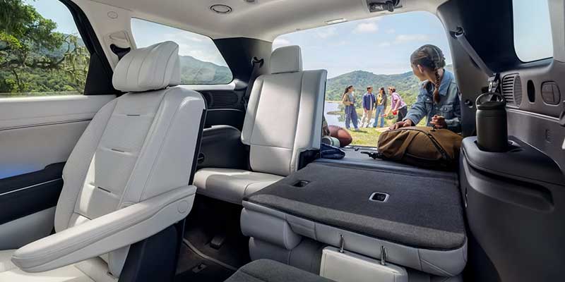 A view from the interior of a Hyundai Palisade SUV, showing spacious seating and an open back door with people in the background near a lake.
