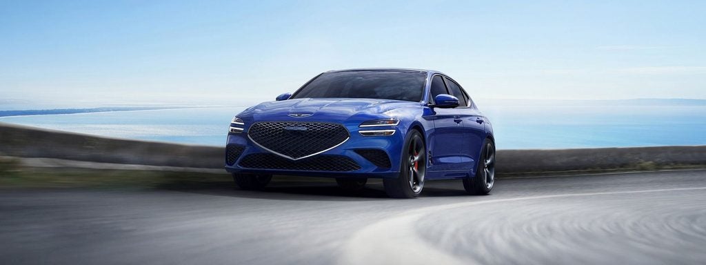 Genesis sedan driving along a coastal road.