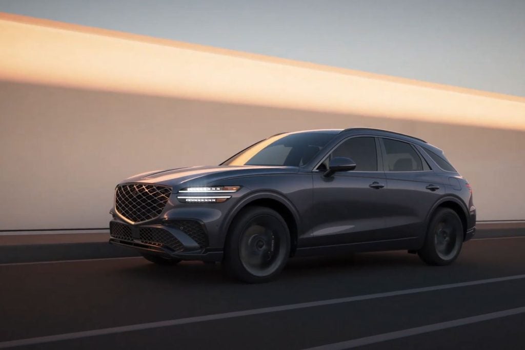 A sleek gray Genesis GV70 SUV parked on a road with a golden light background.