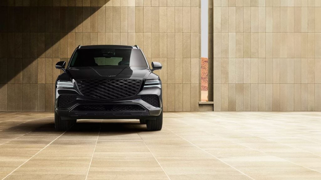 A black Genesis GV80 SUV parked in front of a textured stone wall.