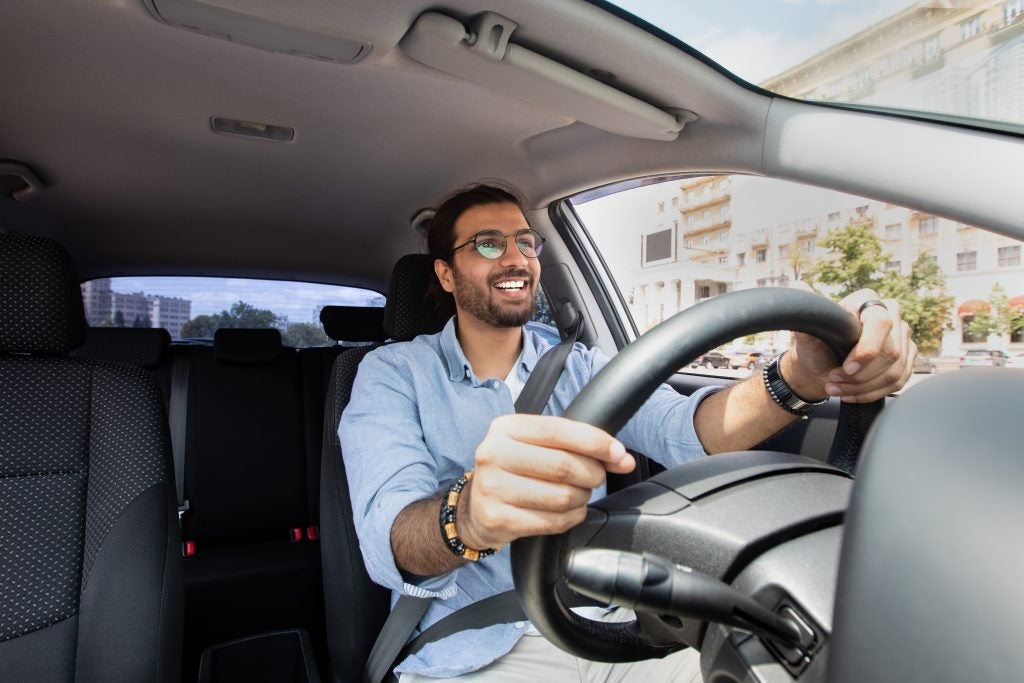 A man driving a car and smiling while holding the steering wheel.