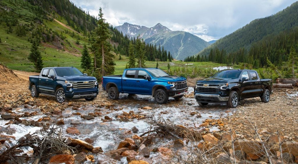 collection of Chevy pickup trucks parked in a stream in the valley of a mountain range