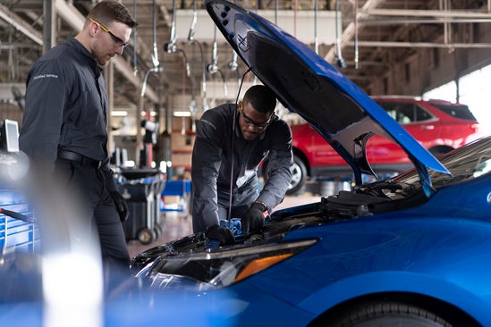 two service technicians looking under the hood of blue Chevy