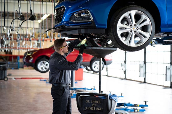 service technician changing the oil of a blue Chevy in a garage at a dealership