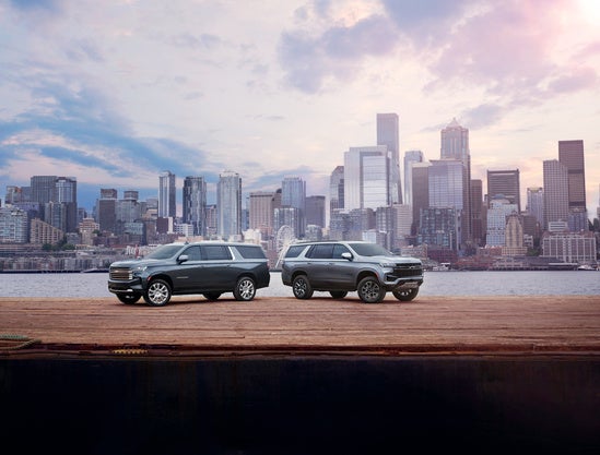 two silver Chevy Tahoes parked in front of the water with NYC in the background
