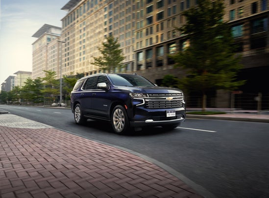 dark blue Chevy Tahoe driving downtown in front of city buildings