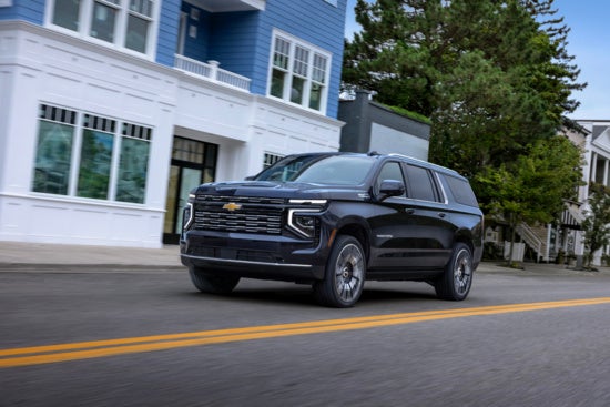 black Chevy Suburban driving past a building downtown