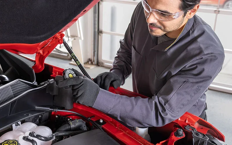 Technician inspecting a vehicle engine under the hood while wearing safety glasses and gloves in a Chevrolet service center