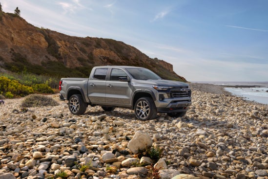 gray Chevy Colorado parked on a stone beach in front of water