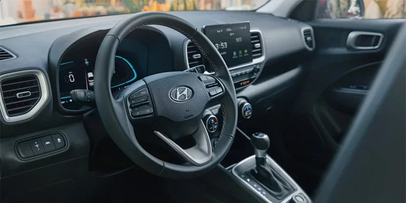 A close-up of the interior of a Hyundai Venue, featuring the steering wheel, dashboard display, and modern controls. The design emphasizes comfort and advanced technology with a clean, user-friendly layout.