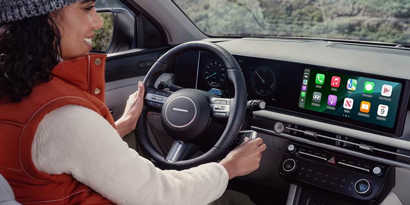 A woman behind the wheel of a Hyundai car, interacting with Apple CarPlay on the dashboard display.