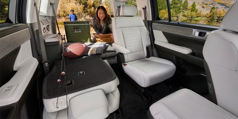 An interior view of a spacious Hyundai Santa Fe with white leather seats and a folded rear seat, showing a woman organizing items in the back. 
