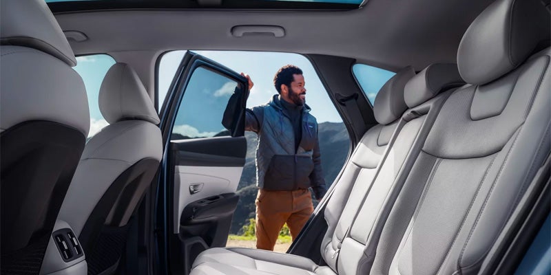 A man stands outside a Hyundai Tucson with the back door open, showcasing a spacious interior with light-colored seats.