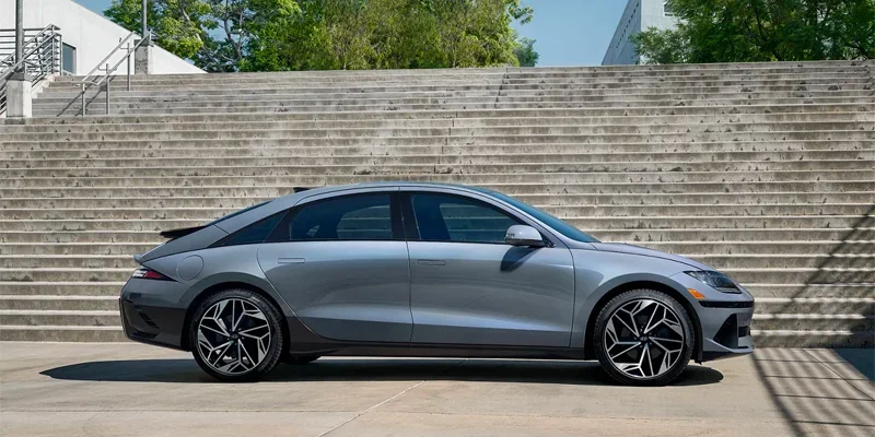 A side view of a sleek, silver Hyundai Ioniq 6 parked in front of a set of concrete stairs, highlighting its modern, aerodynamic design and stylish alloy wheels.