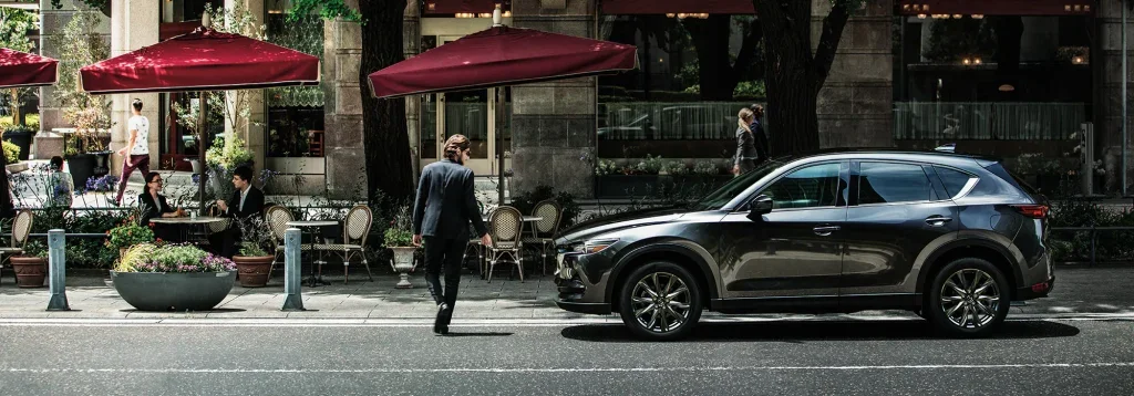man in black suit walking in front of a black Mazda CX-5 parked downtown