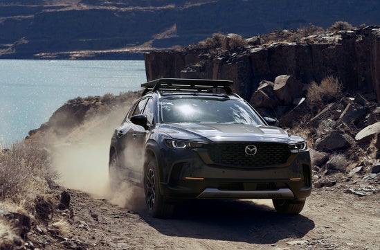 gray Mazda CX-50 driving off road in front of a lake