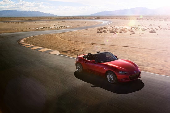 birds eye view of a red Mazda Miata driving on a rural desert road at sunset