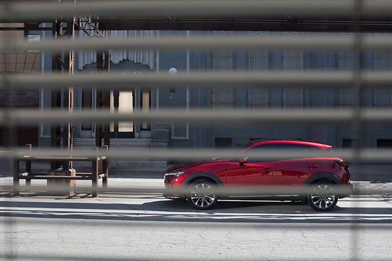 person looking through window blinds at a red Mazda parked downtown
