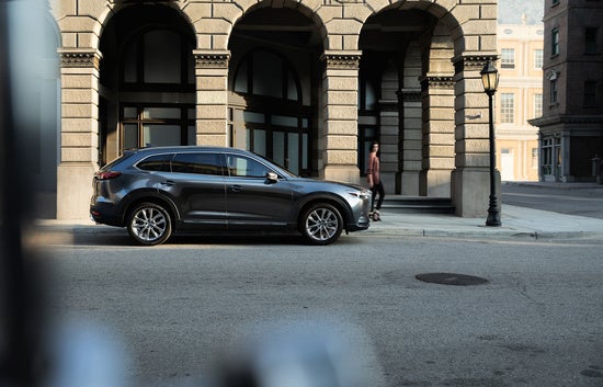 woman walking past a gray Mazda SUV parked downtown in front of a stone building