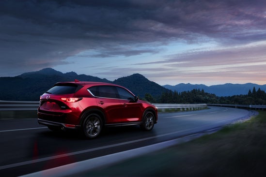 red Mazda CX-5 driving on a rural road at dusk
