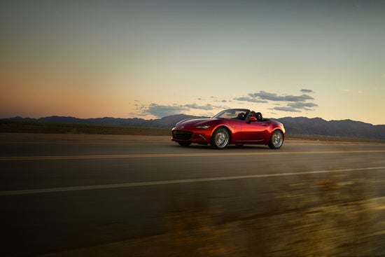 red Mazda Miata driving on a rural desert road at sunset