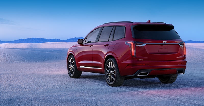 A red Cadillac XT6 SUV parked in a snowy landscape with a clear blue sky.
