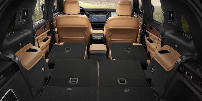 Interior of a Jeep Grand Cherokee with the rear seats folded down, featuring tan leather upholstery and a spacious cargo area.