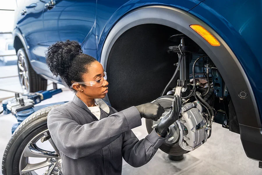 A mechanic working on the brake system of a car, with safety gear on, in a service garage.