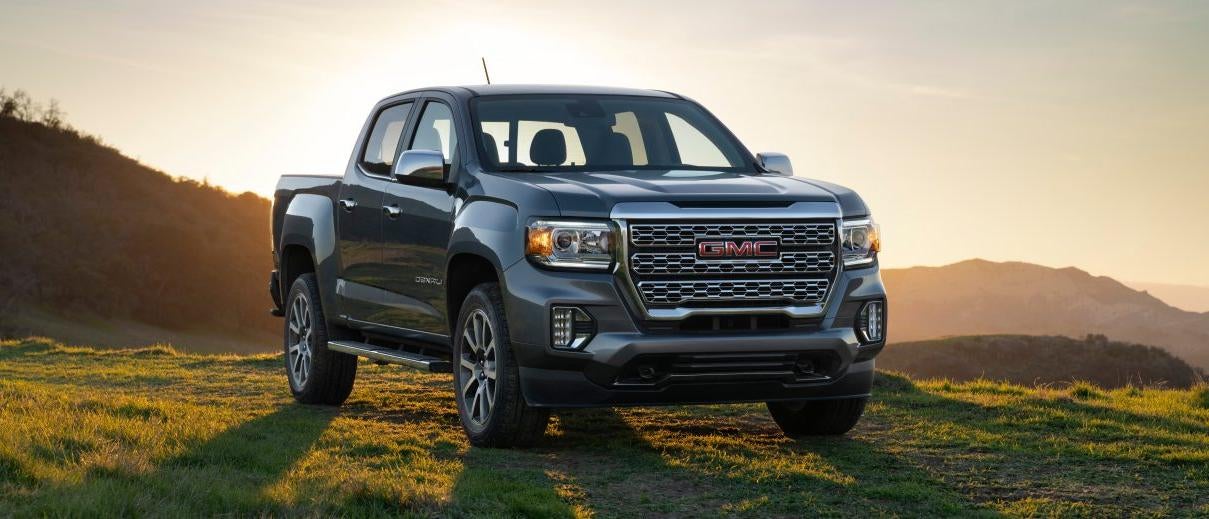 A grey 2023 GMC canyon parked in a field of grass by the mountains