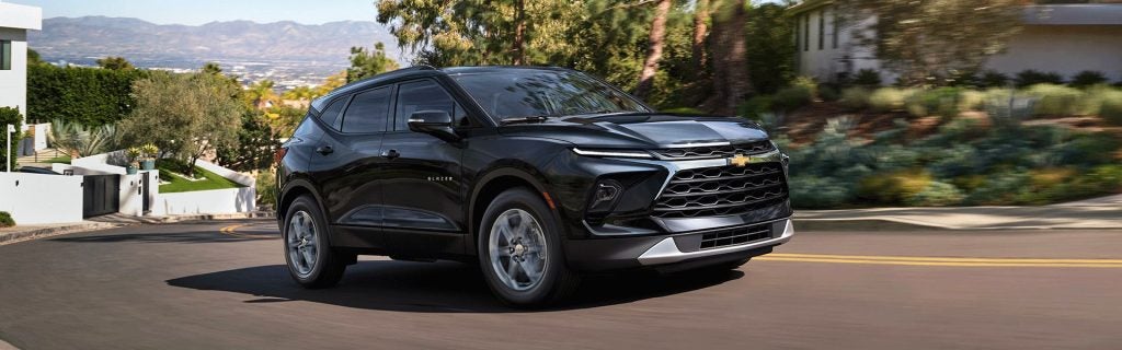 Black Chevrolet Blazer driving on a winding road through a hillside neighborhood.