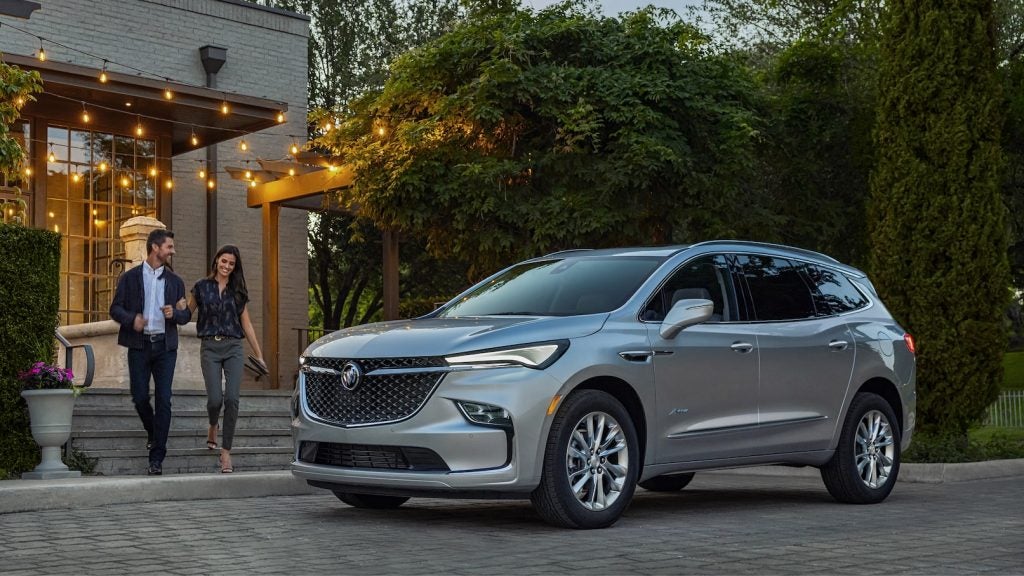 A silver SUV parked in front of a restaurant with a man and woman walking arm in arm toward it.