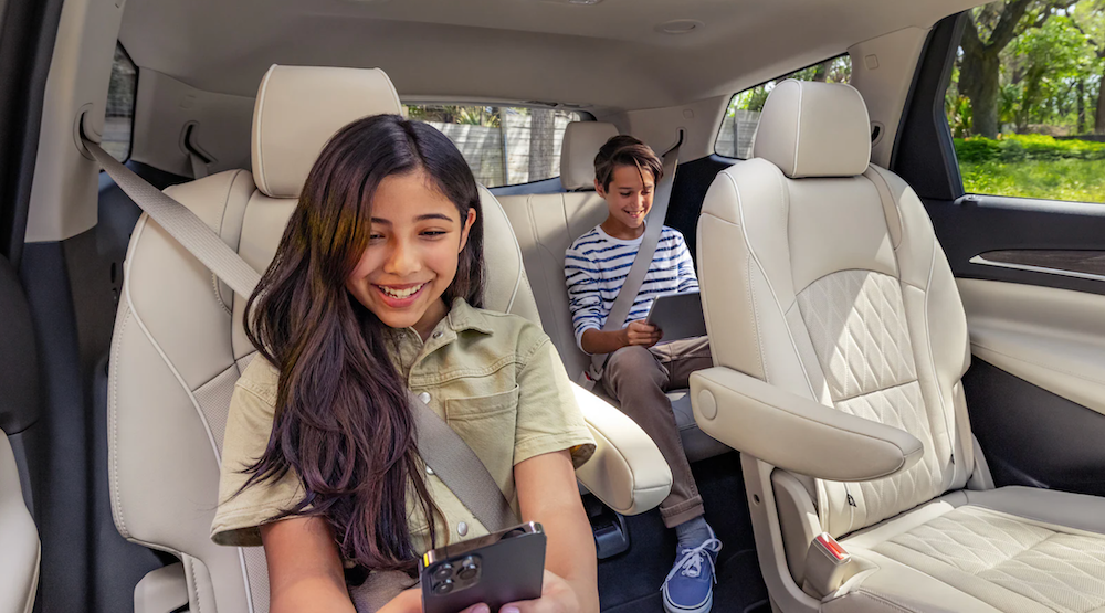 A young boy and a girl buckled into the back seat of an SUV both playing on electronics.